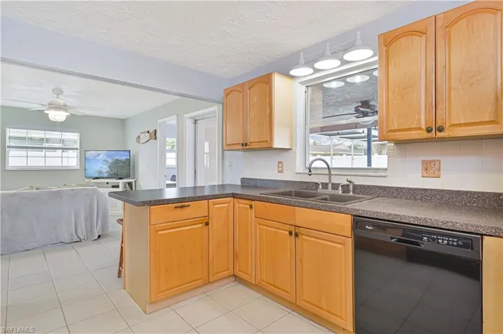 Kitchen featuring a ceiling fan, dark countertops, open floor plan, black dishwasher, and a textured ceiling