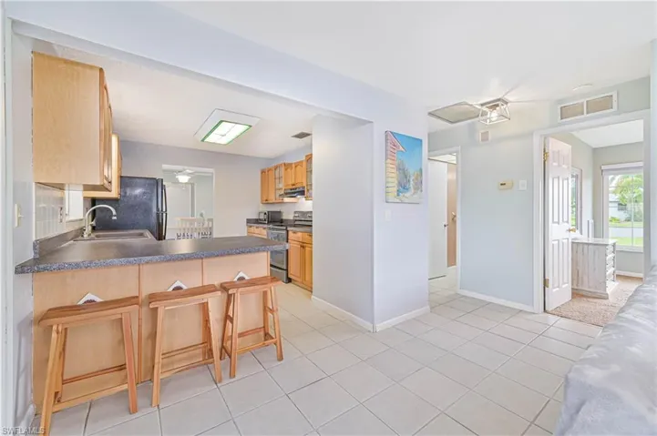 Kitchen featuring electric range, a breakfast bar, dark countertops, light tile patterned floors, and ceiling fan