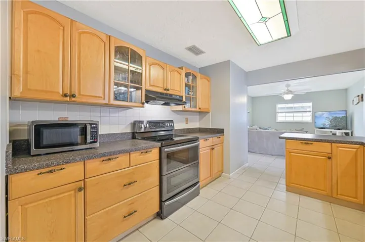 Kitchen featuring stainless steel appliances, glass insert cabinets, dark countertops, open floor plan, and backsplash