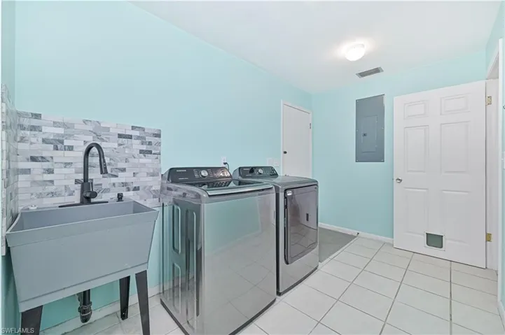 Washroom featuring light tile patterned floors, electric panel, and washing machine and clothes dryer