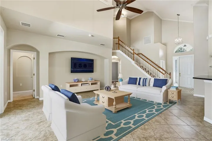 Living room with high vaulted ceiling, arched walkways, ornamental molding, light tile patterned flooring, and a ceiling fan