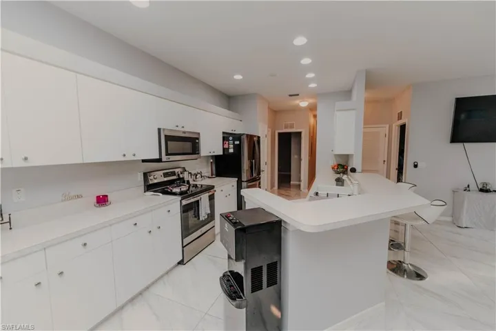 Kitchen with appliances with stainless steel finishes, a breakfast bar, light countertops, white cabinets, and recessed lighting