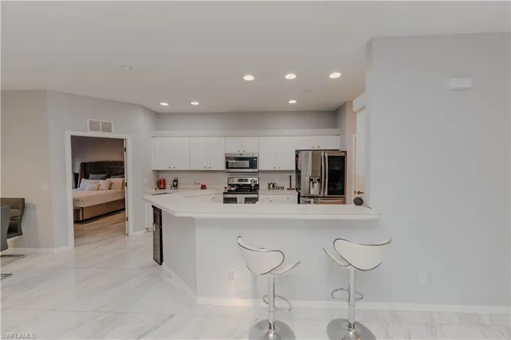 Kitchen featuring a breakfast bar area, stainless steel appliances, light countertops, white cabinetry, and recessed lighting