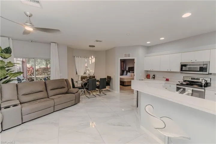 Kitchen featuring light countertops, stainless steel appliances, white cabinets, decorative light fixtures, and open floor plan