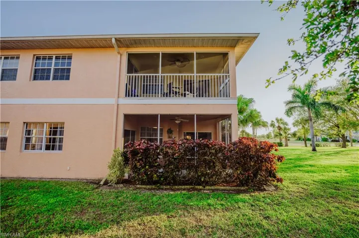 Rear view of property featuring ceiling fan, a sunroom, a lawn, stucco siding, and a balcony