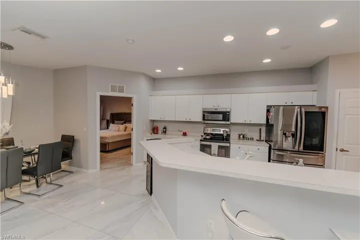 Kitchen with stainless steel appliances, light countertops, white cabinets, pendant lighting, and a breakfast bar area