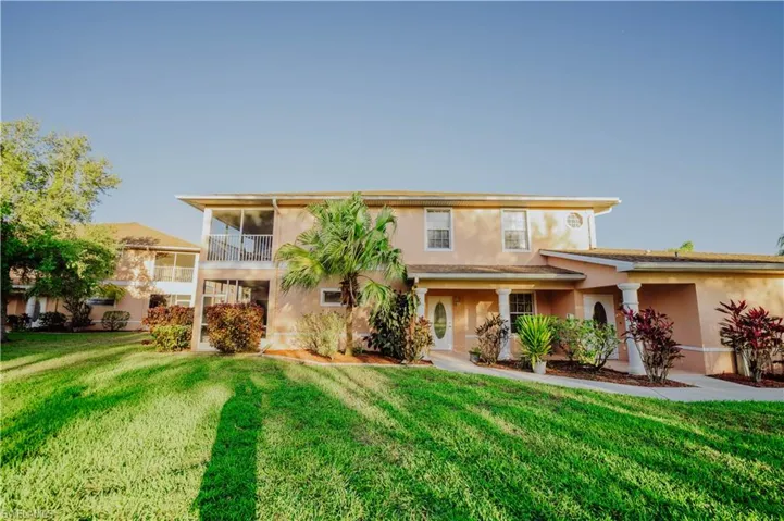 View of front facade featuring a front lawn, stucco siding, and a balcony