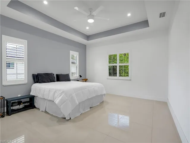 Primary Bedroom with large tile flooring, ceiling fan, and tray ceiling