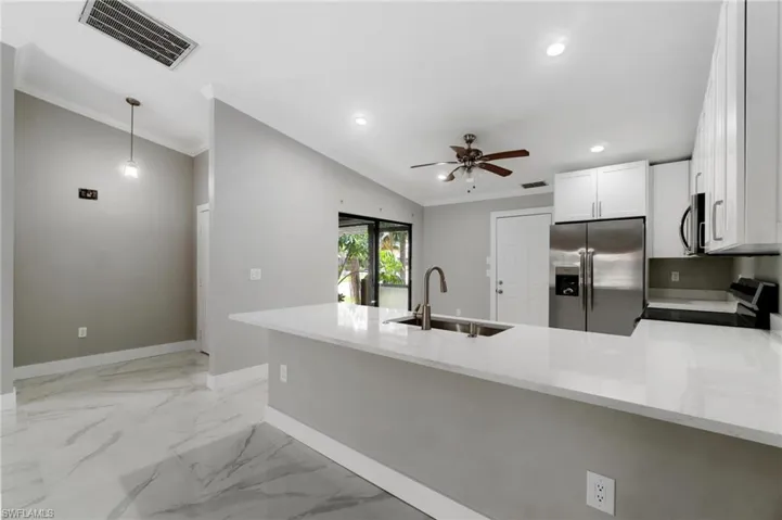 Kitchen with a peninsula, stainless steel appliances, a ceiling fan, light stone counters, and light marble finish flooring