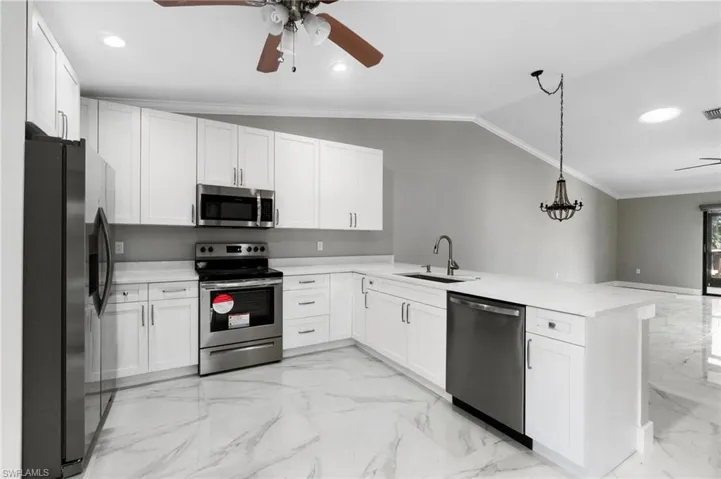 Kitchen with ceiling fan, stainless steel appliances, white cabinets, ornamental molding, and a peninsula
