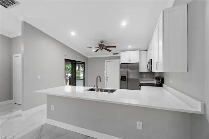 Kitchen featuring a peninsula, light stone countertops, stainless steel appliances, white cabinetry, and light marble finish floors
