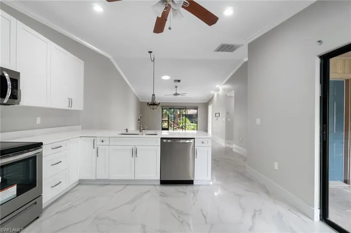 Kitchen featuring ornamental molding, a ceiling fan, white cabinets, stainless steel appliances, and a peninsula