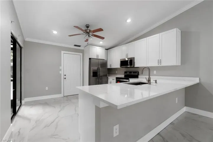 Kitchen with stainless steel appliances, light stone counters, ceiling fan, white cabinets, and a peninsula