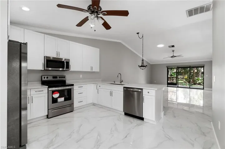 Kitchen with ceiling fan, crown molding, stainless steel appliances, white cabinetry, and a peninsula