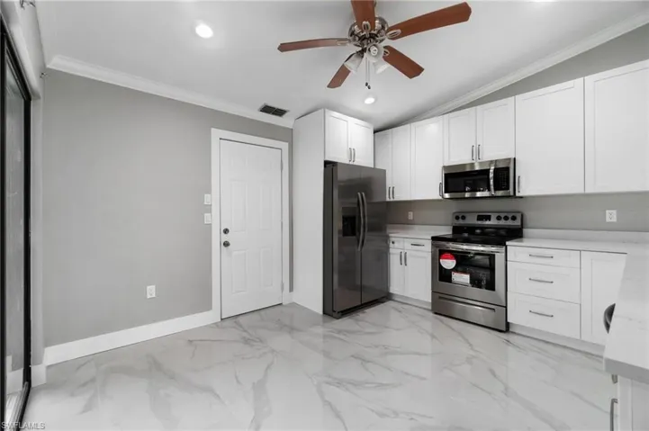 Kitchen featuring stainless steel appliances, ceiling fan, white cabinetry, ornamental molding, and recessed lighting