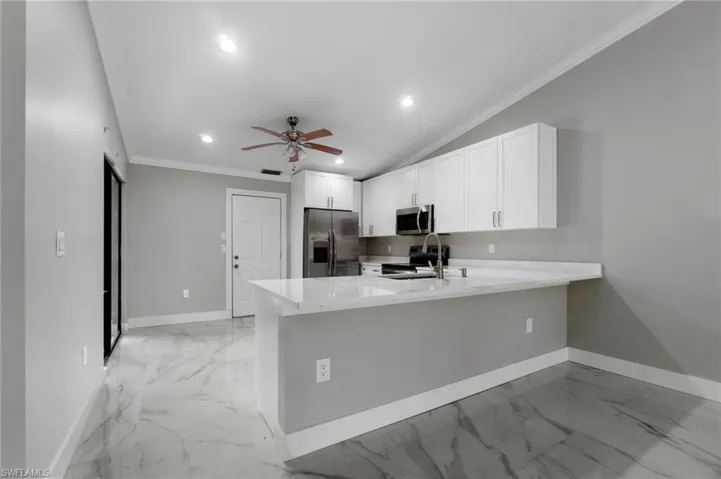 Kitchen featuring white cabinets, ceiling fan, light stone counters, a peninsula, and stainless steel appliances