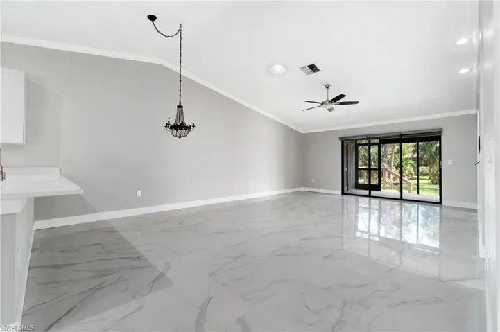 Unfurnished living room with lofted ceiling, crown molding, a ceiling fan, hanging lights, and light marble finish flooring