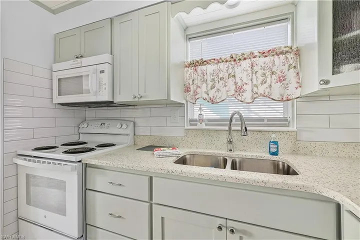 Kitchen featuring light stone countertops, sink, white appliances, and tasteful backsplash