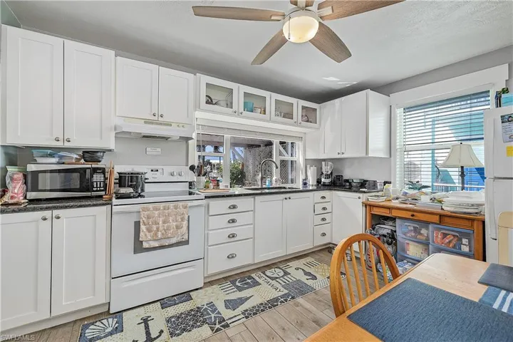 Kitchen with light wood-type flooring, white appliances, ceiling fan, and plenty of natural light