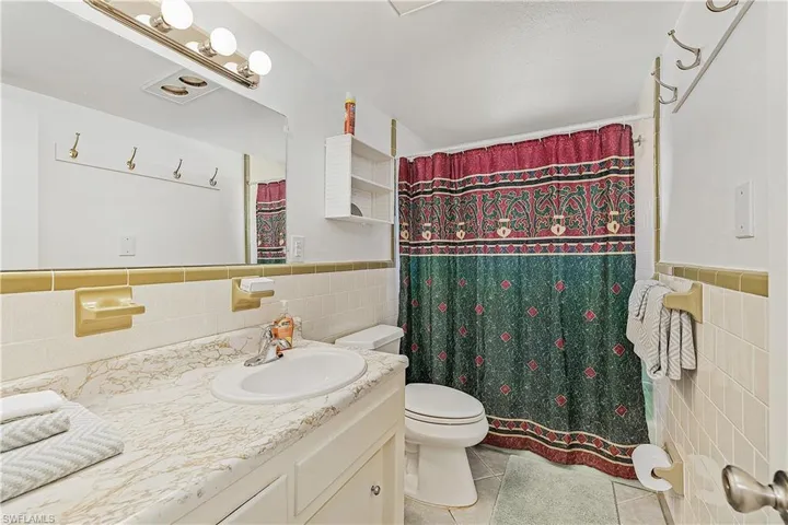 Bathroom featuring tile walls, tile patterned flooring, a shower with curtain, vanity, and toilet