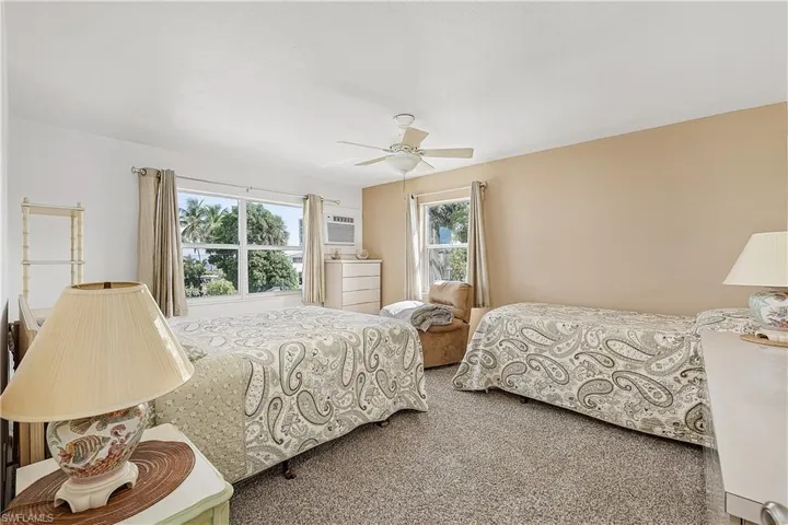 Carpeted bedroom featuring ceiling fan, multiple windows, and a wall unit AC