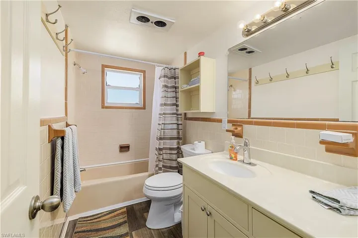 Full bathroom with tile walls, shower / bath combo, hardwood / wood-style flooring, vanity, and toilet