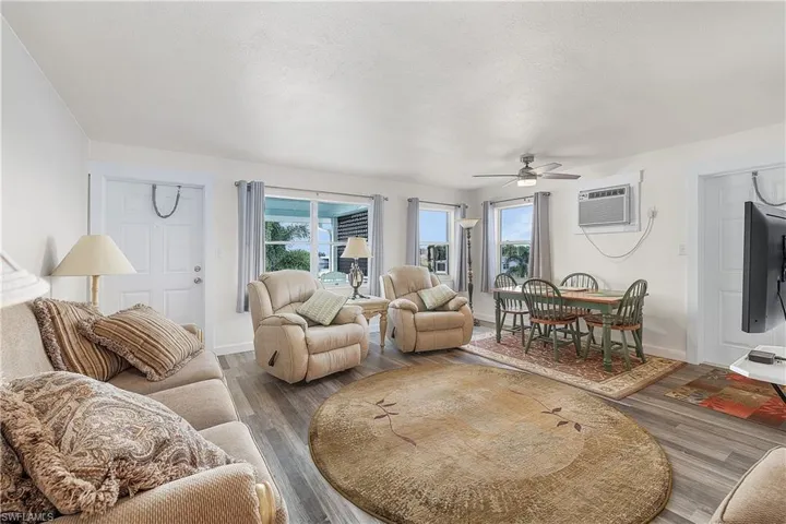 Living room with ceiling fan, a wall unit AC, hardwood / wood-style floors, and a healthy amount of sunlight