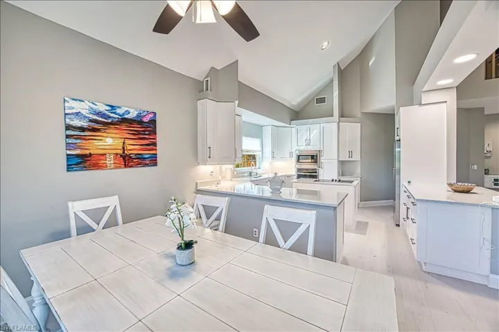 Dining area featuring ceiling fan, high vaulted ceiling, sink, and light hardwood / wood-style floors
