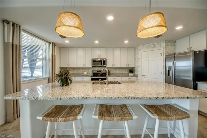 Kitchen featuring a large island, sink, appliances with stainless steel finishes, and hanging light fixtures