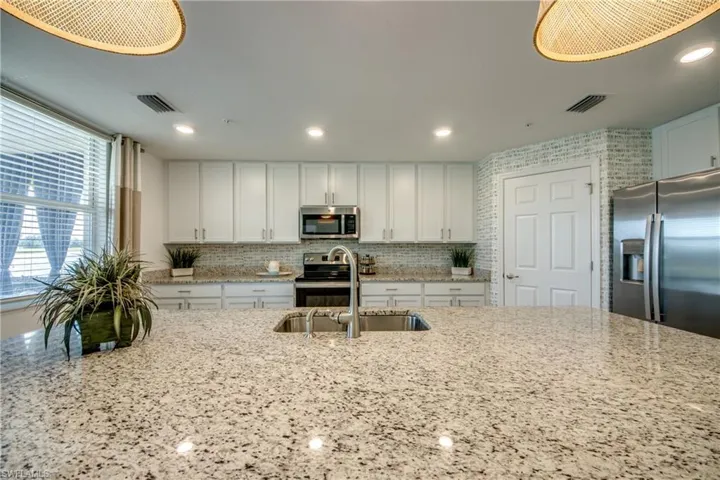 Kitchen featuring decorative backsplash, white cabinetry, light stone countertops, sink, and stainless steel appliances