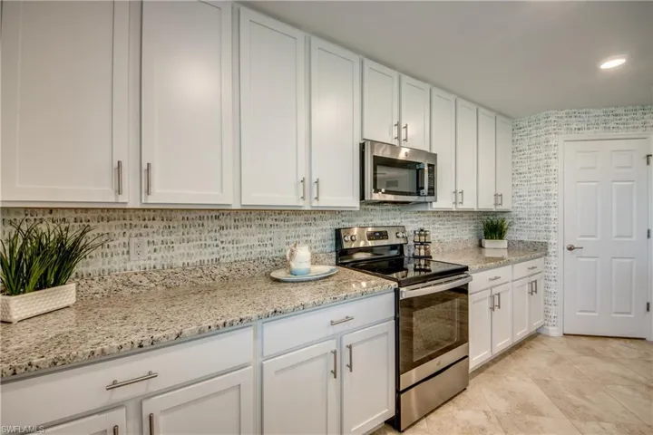 Kitchen with light stone countertops, stainless steel appliances, white cabinets, decorative backsplash, and light tile patterned floors