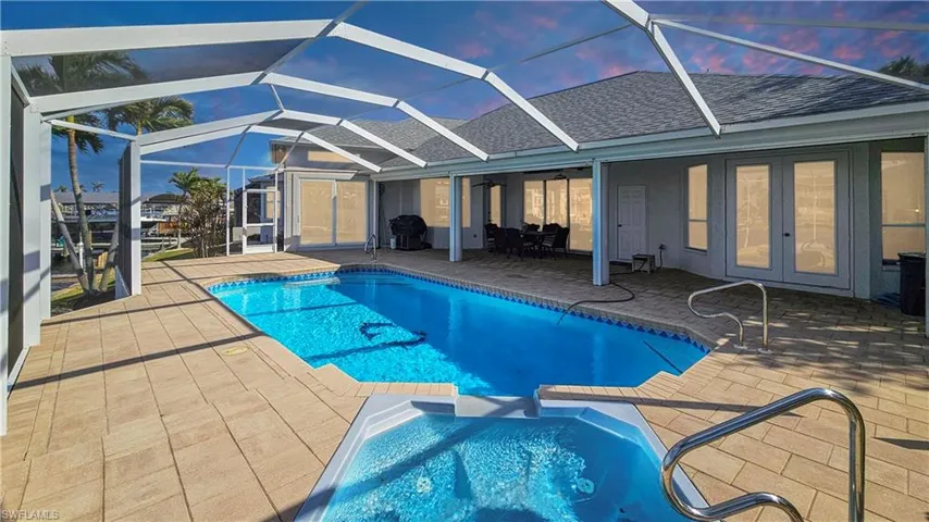Pool at dusk with a patio, ceiling fan, and glass enclosure