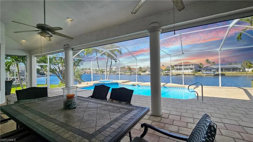 Patio terrace at dusk with a water view, ceiling fan, a pool with hot tub, and glass enclosure