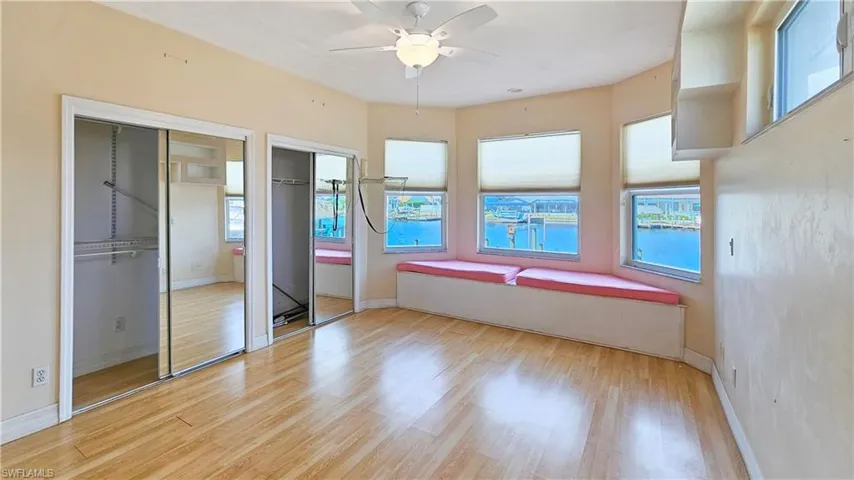 Unfurnished bedroom featuring multiple windows, ceiling fan, two closets, and light wood-type flooring