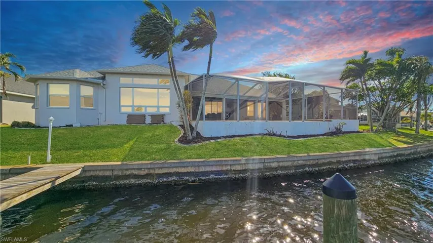 Back house at dusk with a yard, a lanai, central AC, and a water view