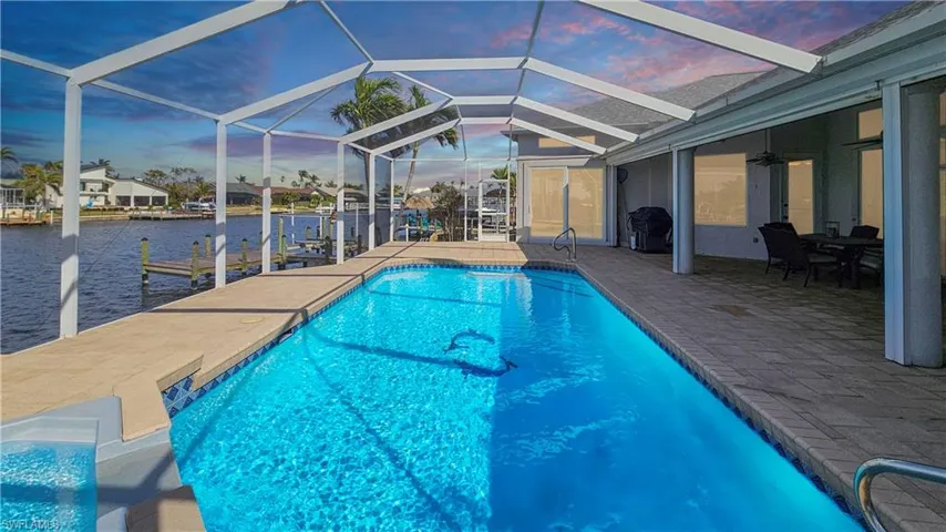 Pool at dusk featuring a patio, a lanai, ceiling fan, a water view, and a dock