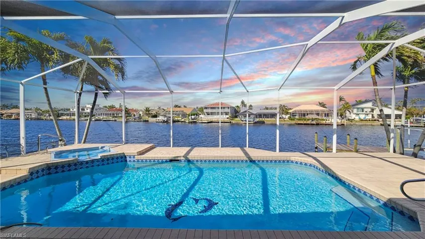 Pool at dusk featuring a water view, an in ground hot tub, a boat dock, and a lanai