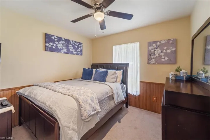 Bedroom featuring wainscoting, wood walls, a ceiling fan, and light colored carpet