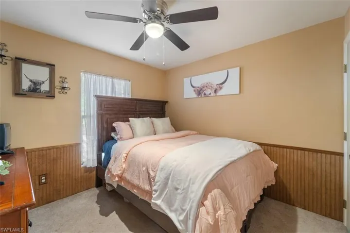 Bedroom featuring wood walls, wainscoting, a ceiling fan, and light colored carpet