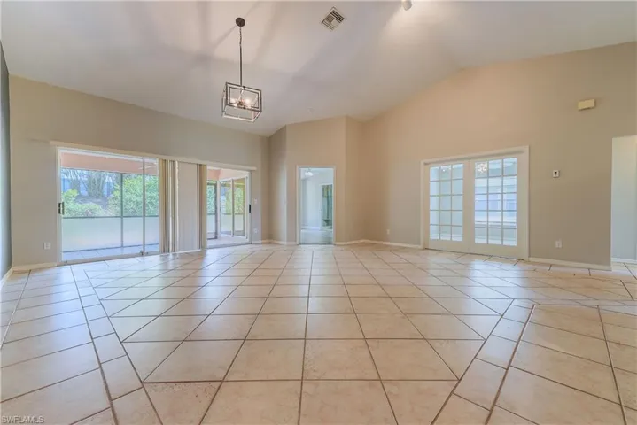Empty room with a chandelier, light tile patterned floors, baseboards, and high vaulted ceiling