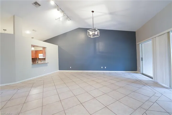 Empty room featuring track lighting, lofted ceiling, light tile patterned floors, baseboards, and a chandelier