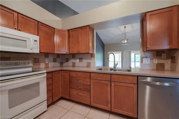 Kitchen featuring white appliances, a sink, brown cabinets, decorative backsplash, and lofted ceiling