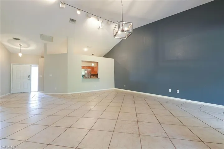 Spare room featuring track lighting, light tile patterned flooring, baseboards, and high vaulted ceiling