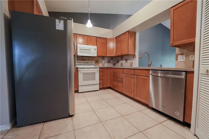 Kitchen with stainless steel appliances, backsplash, a sink, light countertops, and brown cabinetry
