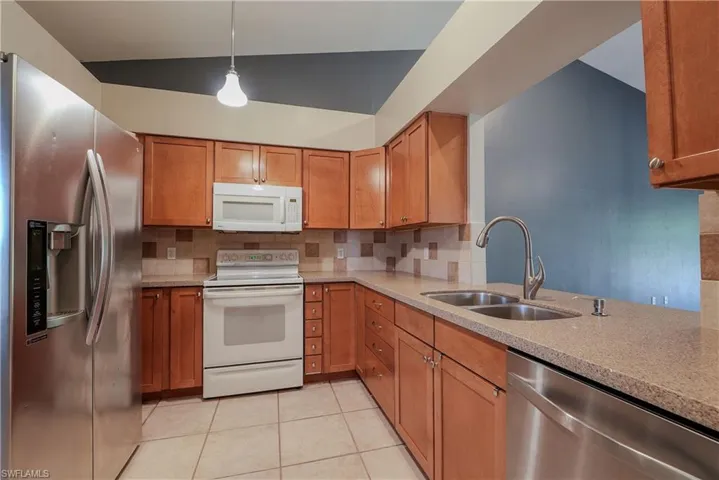 Kitchen with stainless steel appliances, a sink, brown cabinetry, and lofted ceiling