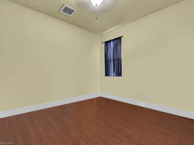 Spare room with dark wood-style flooring, baseboards, and visible vents