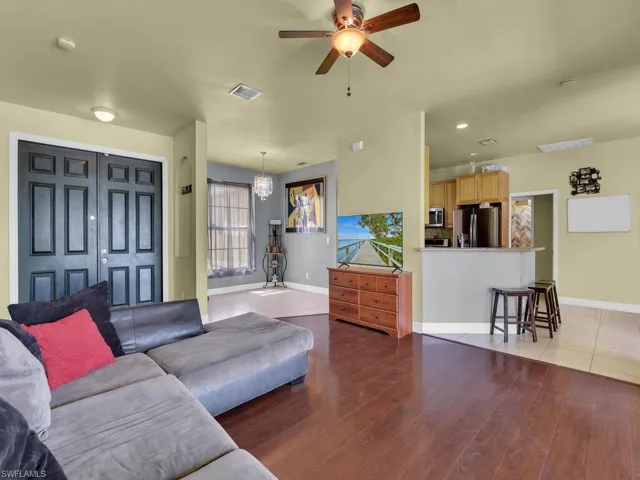 Living area featuring visible vents, baseboards, wood finished floors, and ceiling fan with notable chandelier