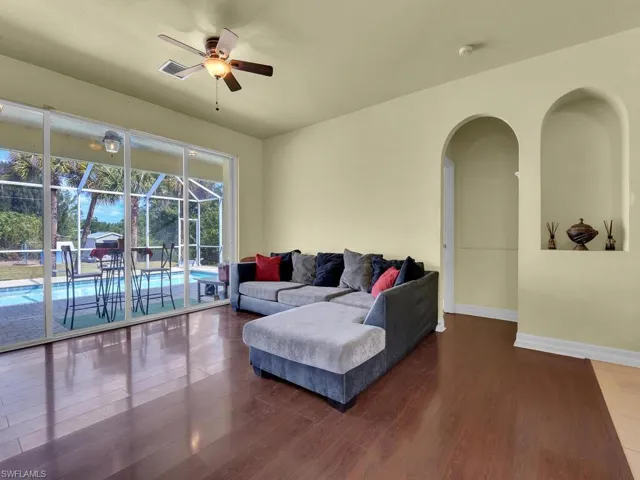 Living room with baseboards, a ceiling fan, visible vents, arched walkways, and wood finished floors