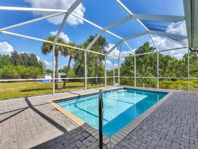 Pool with a patio area, glass enclosure, and a yard