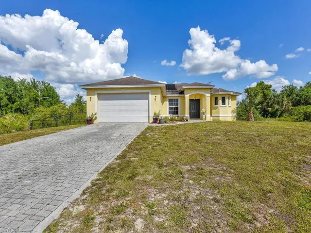 View of front facade with an attached garage, fence, stucco siding, a front lawn, and decorative driveway